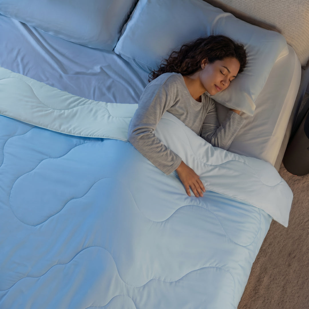 Woman sleeping under a light blue cooling comforter from an overhead view